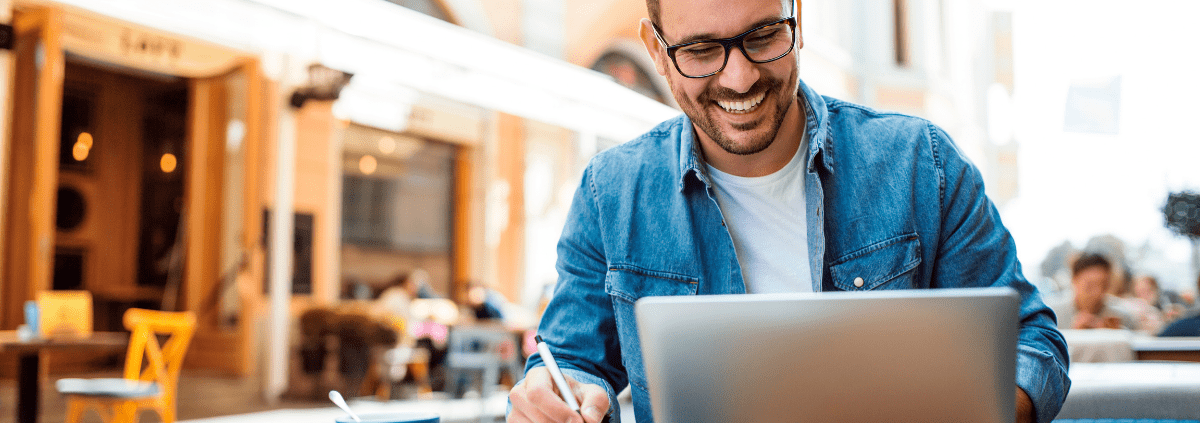 man sitting with laptop smiling at a coffee shop